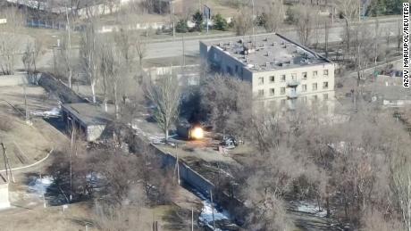This screenshot from drone footage shows a military vehicle firing gunshots near a building.